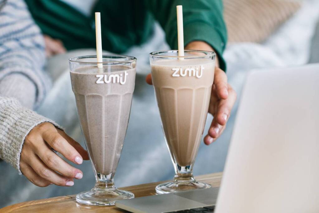 Milkshakes Zumit con tecnología IQF en manos de personas, encima de una mesa