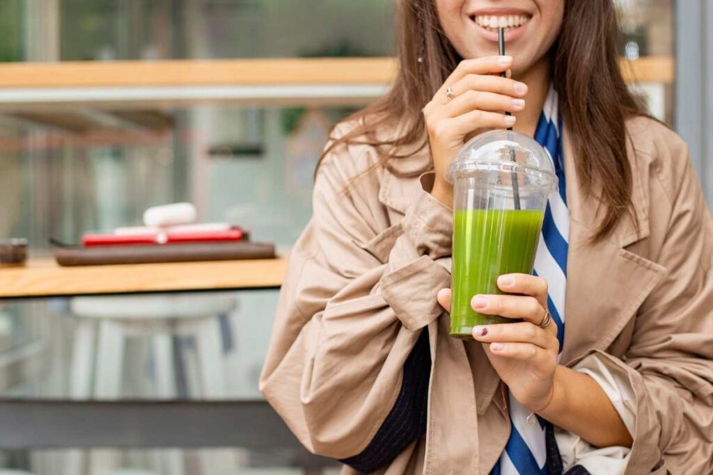 zumo verde detox en las manos de una chica mientras lo ingiere con una pajita negra