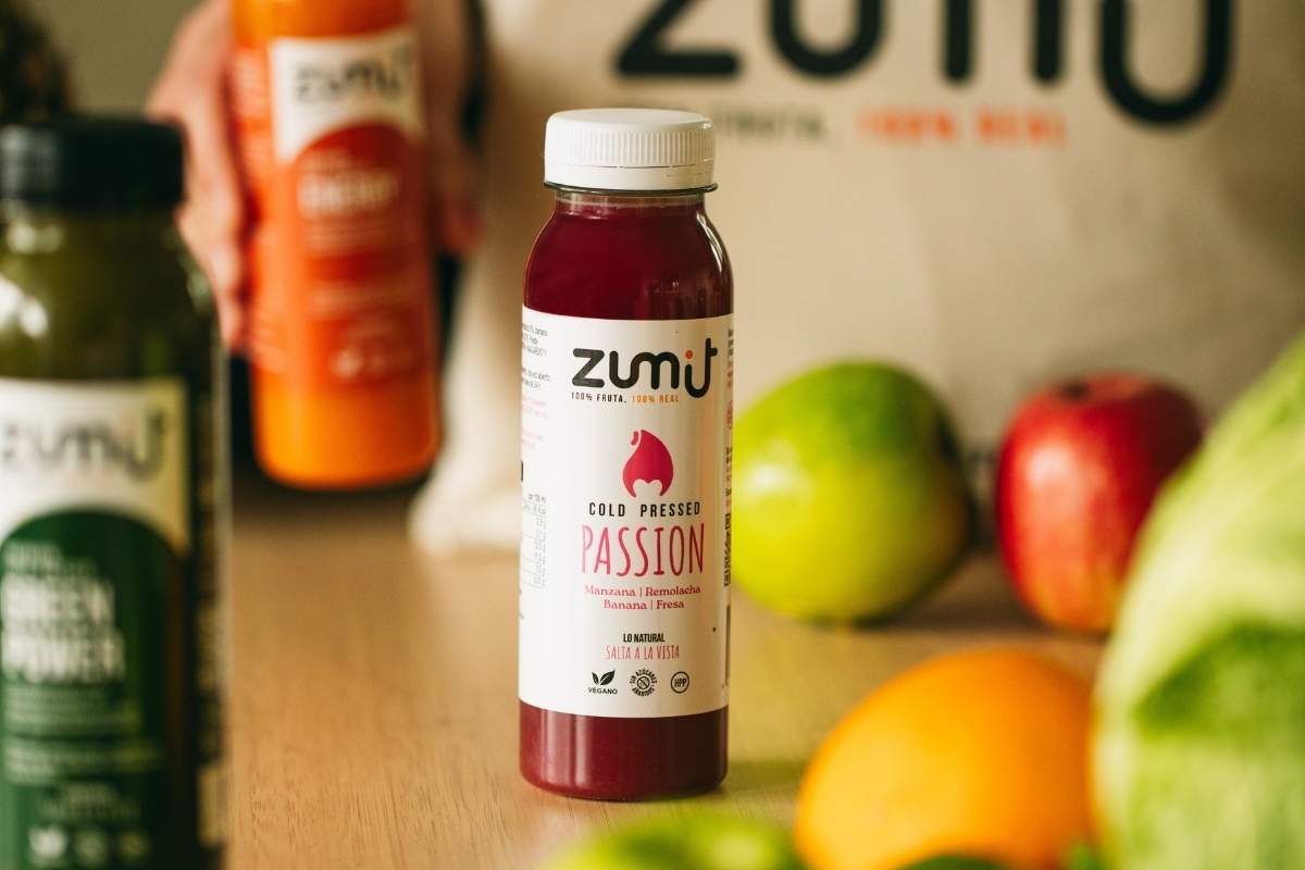 Zumo cold pressed Passion de Zumit en una mesa de madera rodeado de frutas