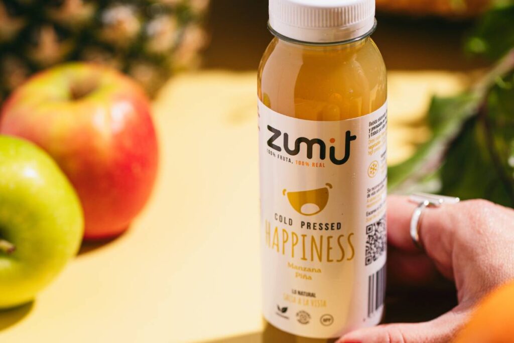 Zumo Cold Pressed Zumit Happiness con manzana y piña sobre una mesa